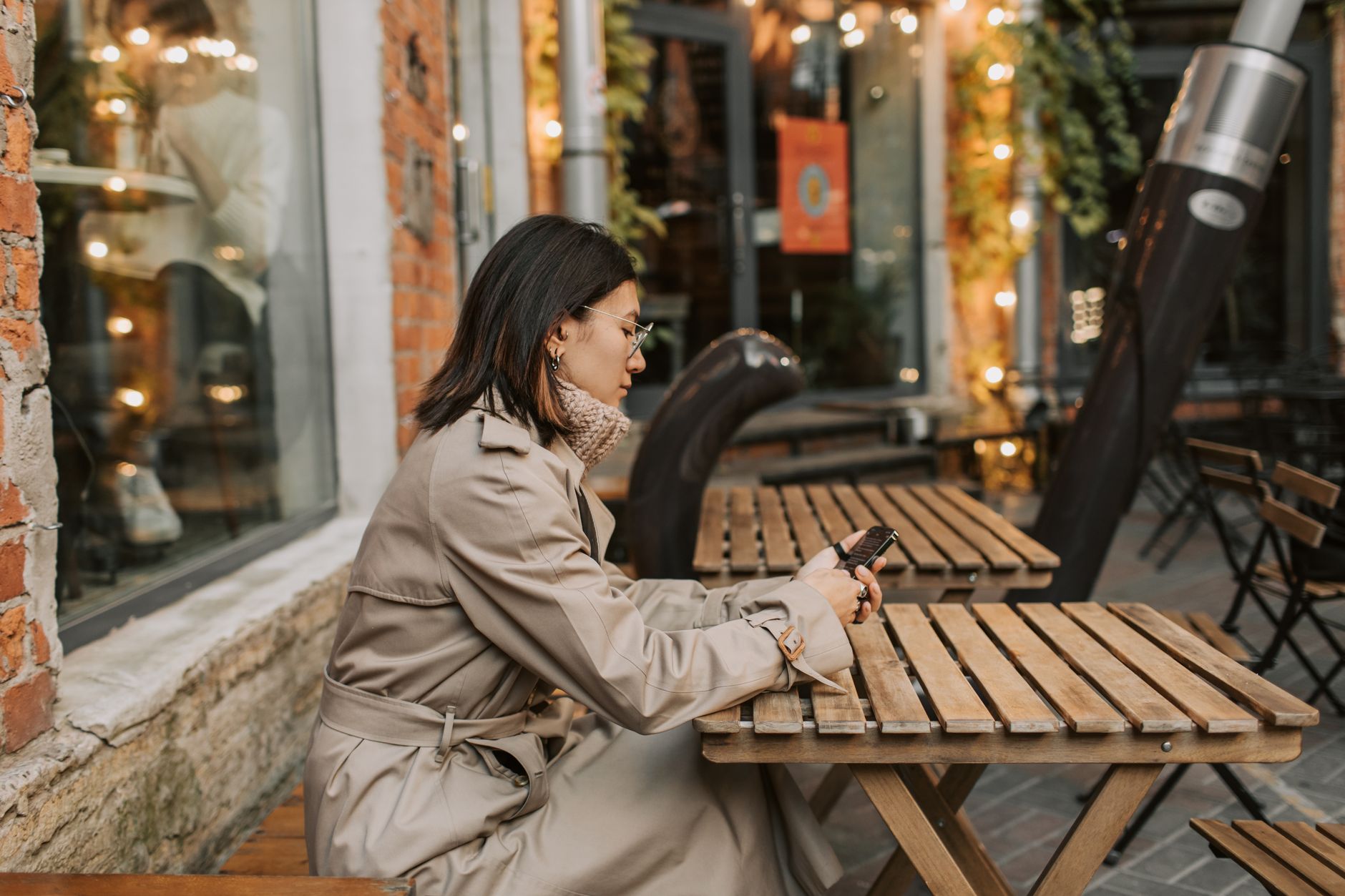 Vrouw in trenchcoat met haar telefoon op een terras