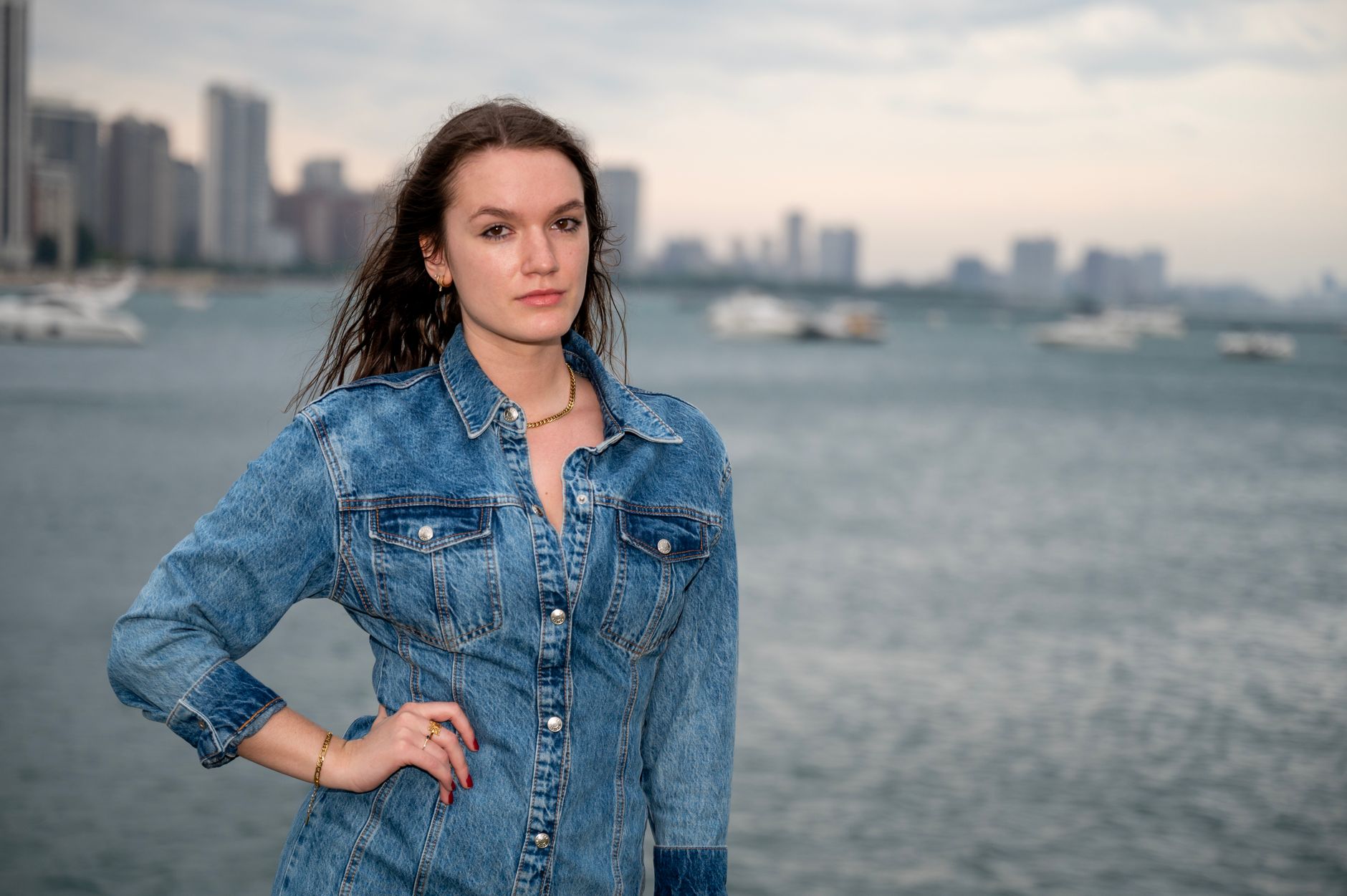 Vrouw in spijkerjas aan het water met de stad op de achtergrond